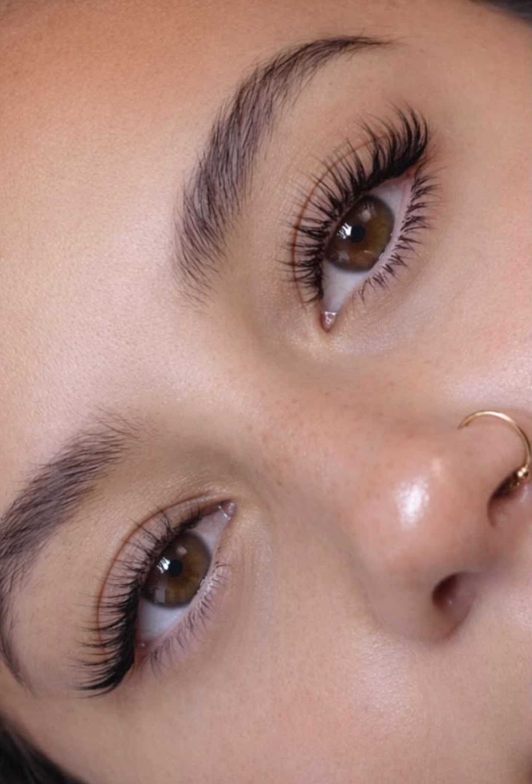 Gros plan de deux yeux bruns aux cils longs, fournis et recourbés, sourcils naturels brossés.