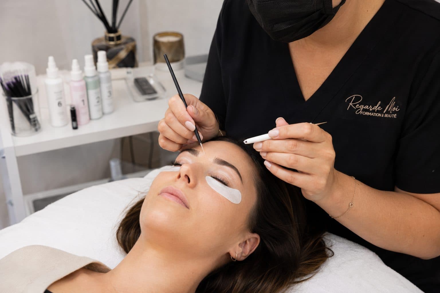 Application des lotions de rehaussement au pinceau fin sur les cils d’une cliente, à l’institut REGARDE MOI.